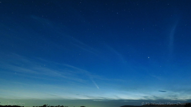 A photo of the night sky not long after sunset. The sky is still quite light, and streaks of wispy cloud are visible. Many stars can be seen at the top of the shot and, near the lower centre, a bright object with a long diagonal trail behind it. This is the comet.