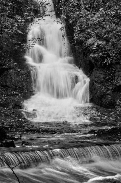 Closer view of water pounding down a waterfall into a pool where it then creates a lovely arcing ribbon of water across the burn