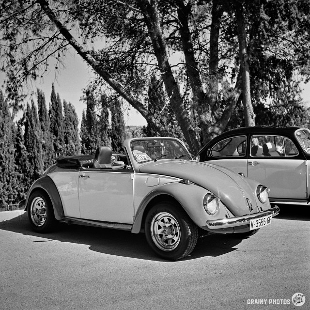 A black-and-white film photo 8:30 two-tone Volkswagen Beetle convertible.