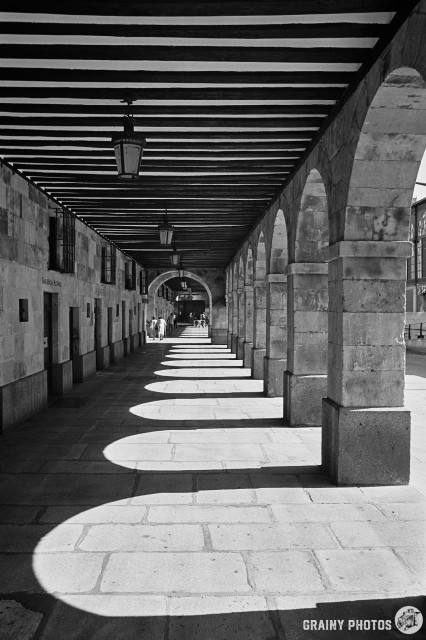 A black-and-white film photo of an arcade with a series of arches along the side of the market in Salamanca Spain.