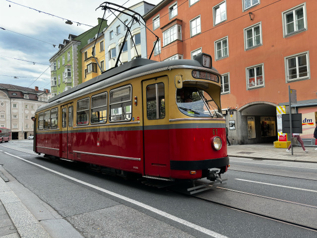 Das Foto ist im Querformat und in Farbe aufgenommen worden. Es ist eine alte Tramgarnitur zu sehen. Die Farben der Tram sind unten rot und oben beige. Außer dem Fahrer und einem Kontrolleur ist sonst niemand in der Straßenbahn zu sehen.