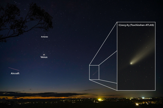 Looking out across the horizon over the city lights, where the night sky is filled with stars, the planet Venus, a faint comet and an aircraft trail. There is an inset of the comet, zoomed in. It shows the intricate details of the comet. Several objects in the image, such as the aircraft, Venus and Antares are also annotated. 