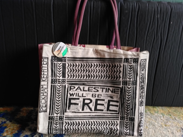 A hemp shopping bag to which has been pinned a Peckham Keffiyeh design saying 'PALESTINE WILL BE FREE' with  FREE PALESTINE badge in the flag colours (faded red since it's pretty old).