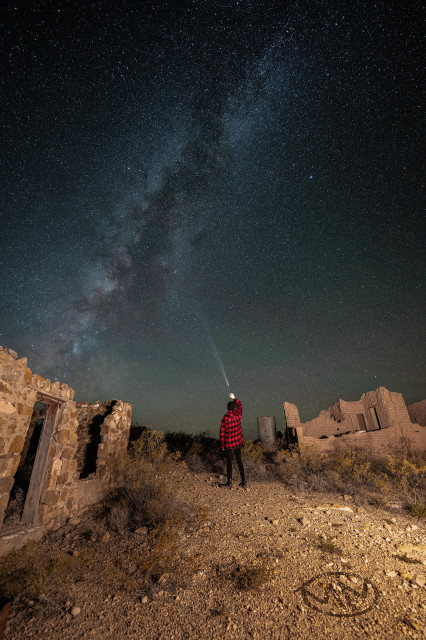 A figure under the milky way reaching up to grab a comet in the ruins of an old ghost town. 