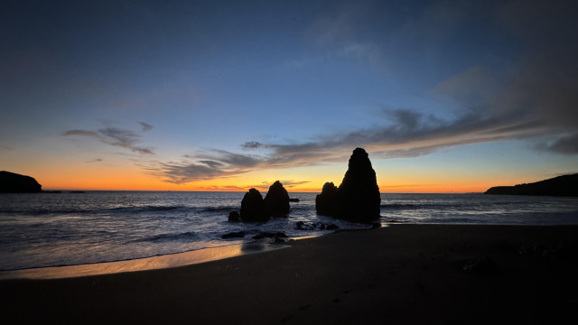 dusk at rodeo lagoon, two rocks stick out at the surf line, the sky behind is orange at the horizon and deep blue at the top