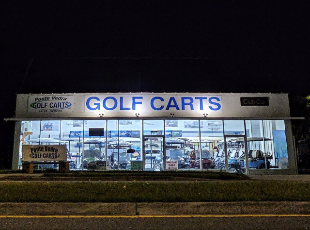 Late night zoom across a roadway where a small, brightly illuminated "Golf Cart" business glows beneath the dark night sky. Golf Carts are a preferred mide of transportation for Florida snowbirds!