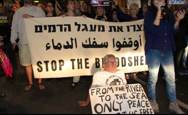 Sign says “stop the bloodshed” in Hebrew, Arabic and English. The elder on the ground is wearing an Israeli Black Panthers party and the sign says “from the river to the sea, only peace will set us free”