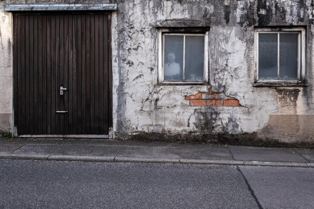 Eine alte, ranzige Hausfassade. Links ein Garagentor, rechts davon 2 Fenster.