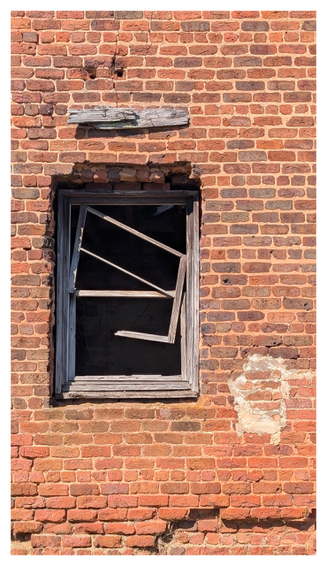 outside wall of a old red brick building with a wood-framed window with no glass.