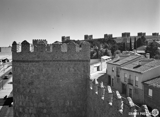 A black-and-white film photo of the city walls with houses in the town on the right-hand side