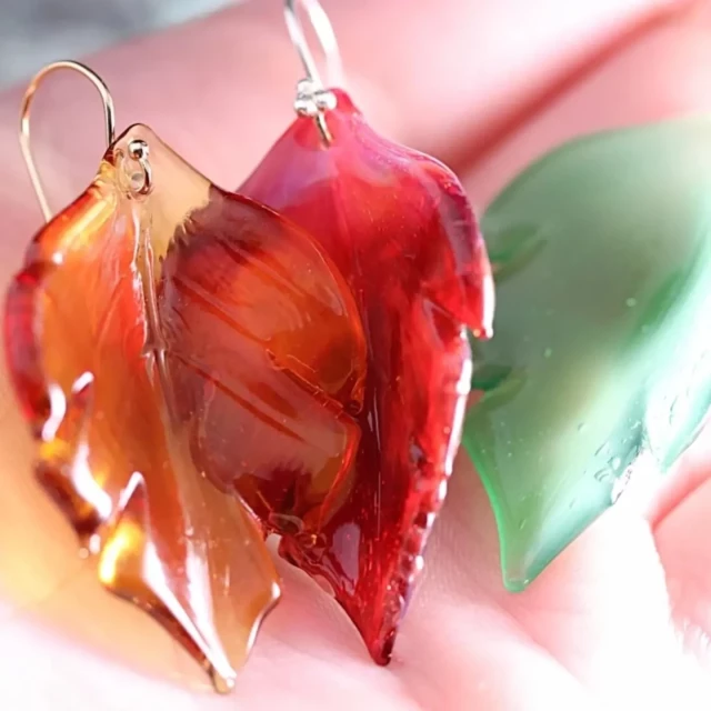 Trois boucles d'oreilles de couleur, rouge, jaune et vert posé sur la mains de la créatrice.