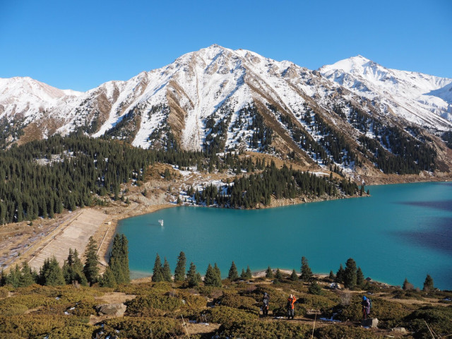 A blue lake with snowy mountains in the background. The sky is blue and clear.