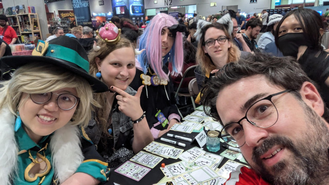 Group of smiling players around a table at MCM Comic Con London where they played Magic of Inventorying 