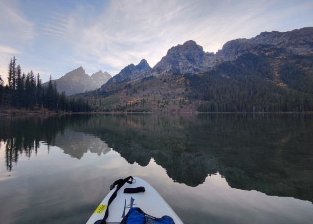 The nose of my paddle board, and the mirror image of the trees and mountains reflected back onto the water. The water is very, very still.