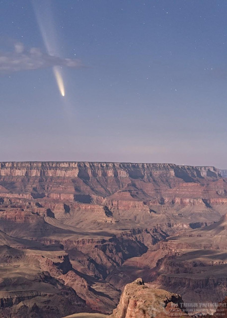 Color photo of a comet pointing down toward the bottom right of the image with a long fuzzy tail going up toward the left top of the image. Part of the comet's tail is obscured by a small cloud. The comet is seen over the Grand Canyon which is a very rough and rugged canyon made up primarily of red and beige sandstones.