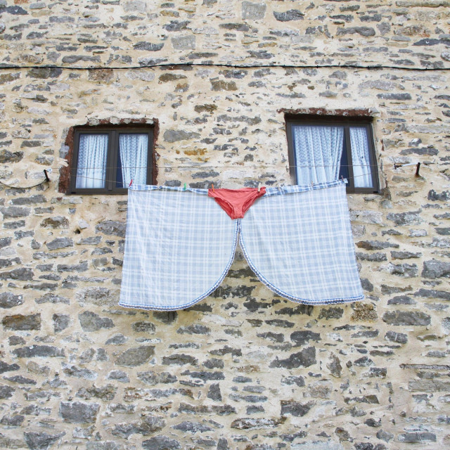 two white garments and pink underwear draped over a clothesline between two windows to look like a cat's face