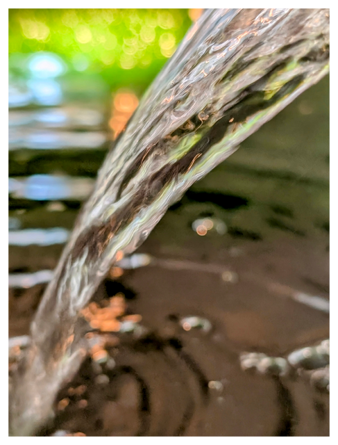 close-up. a stream of water falls from the upper left corner into a pool below, creating circles. 