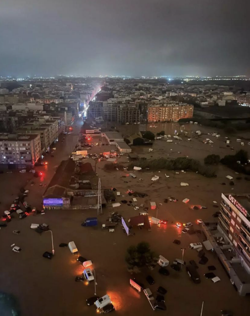 Blick von oben auf Stadt im Halbdunkeln. Alle Straßen stehen unter Wasser, viele Autos sind im Wasser, Lichter leuchten gespenstisch.