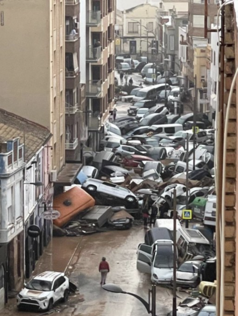 Eine Straße ist in der Flucht zu sehen. Sie ist gefüllt mit angeschwemmten Autos, die sich zu Haufen ballen. 