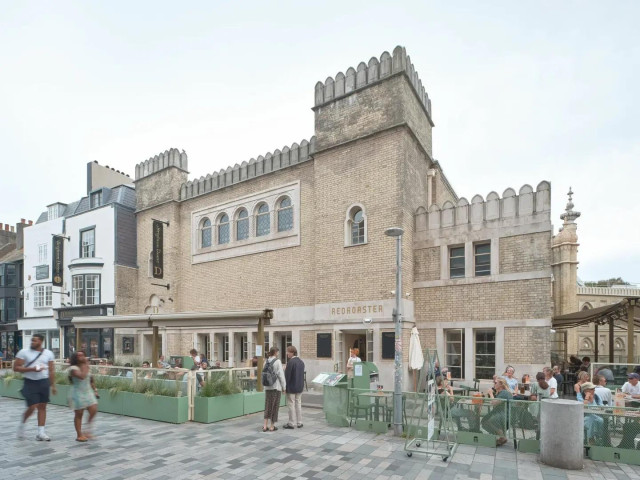 Ornate regency building on a pedestrian street. Lettering on the building says 'Brighton Dome' and 'Redroaster'. People sit at tables outside and drink coffee. Others walk past.