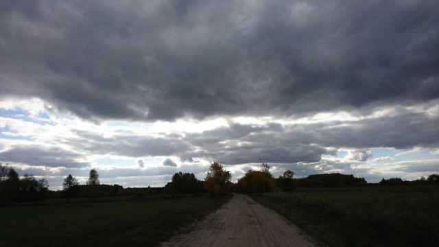 A dirt rural road, heavy dark clouds above.