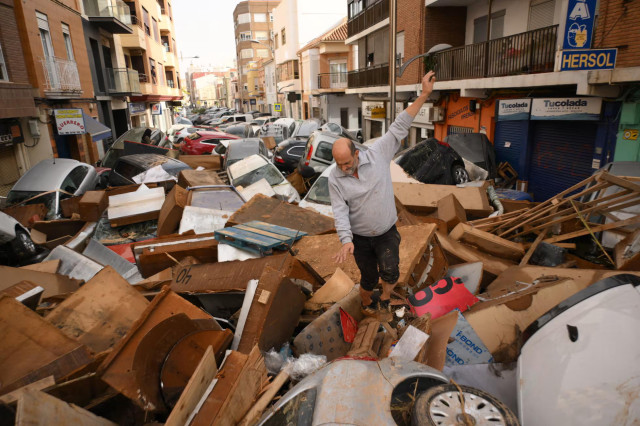 The same street with a mass of debris and cars and a man trying to walk over it all. The same blue tall sign is visible.