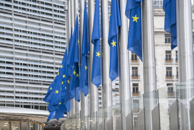 A series of European flags at half mast in front of the facade of the Berlaymont building in Brussels.