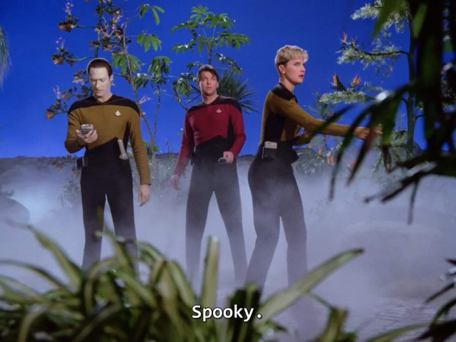 Tasha Yar, Riker, and Data stand outside, with some greenery in the background, a questionably perfect blue sky backdrop, and lots of fog. Yar and Riker have a defensive posture, Data is staring at his phone. (It's a tricorder). Caption reads, "Spooky "