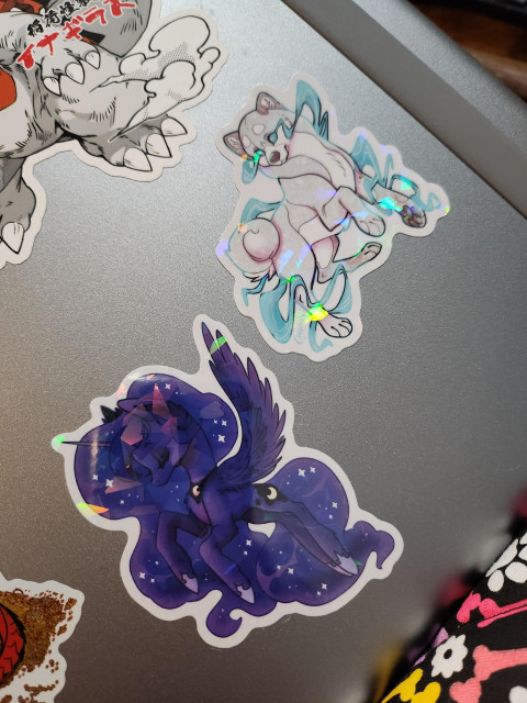 Photo of 2 slightly holographic stickers. Sticker on leg dark Alicorn with moon theming (luna from my little pony). On the right blue and grey spirit like shina inu type dog