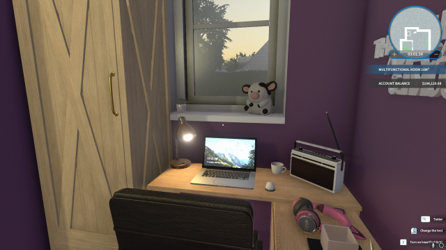 Closeup of the gaming desk. There is a laptop on it and a radio. A cow plushie sits on the windowsill 