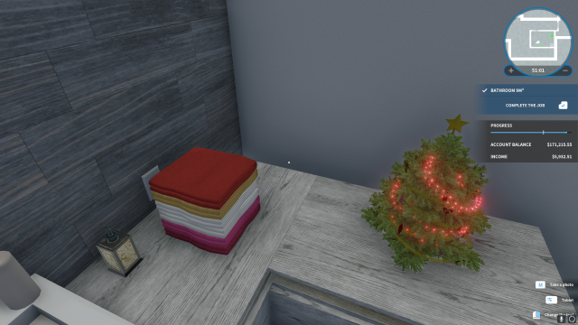 House Flipper screenshot from a bathroom. The main focus of the picture is a stack of towels colored like a lesbian flag. There is a Christmas tree next to it and a bottle of soap on the other side.