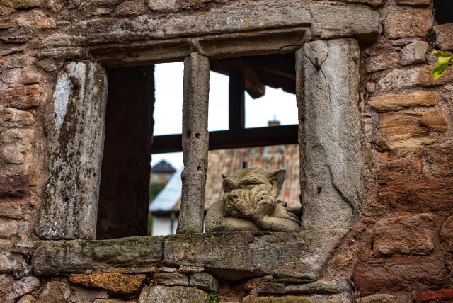 Ein Sandsteingewände in einem alten Gemäuer. Aus dem Fenster schaut ein gelangweilter Gargoyle heraus.

A sandstone wall in an old building. A bored gargoyle looks out of the window.