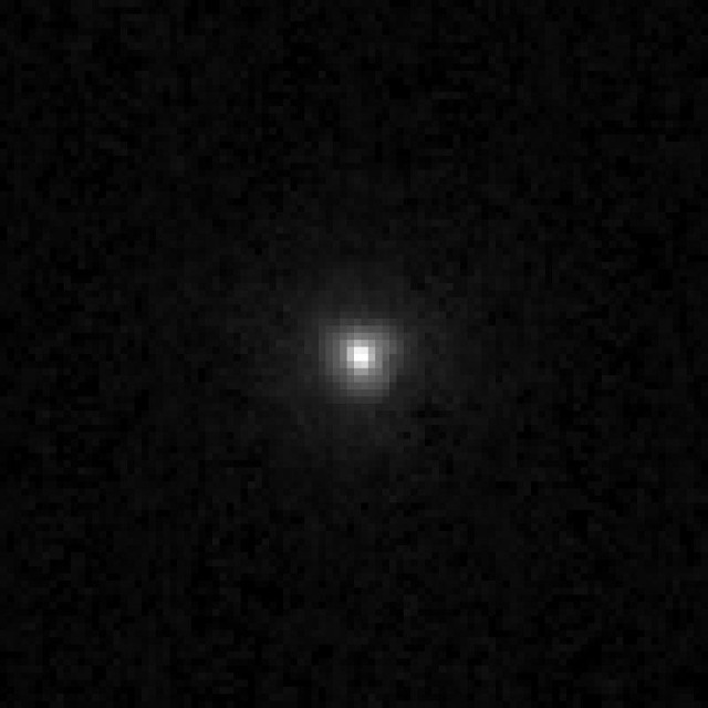 A bright, white round object is seen in the center of this mostly dark image. The object is surrounded by a faint halo of less bright material. 