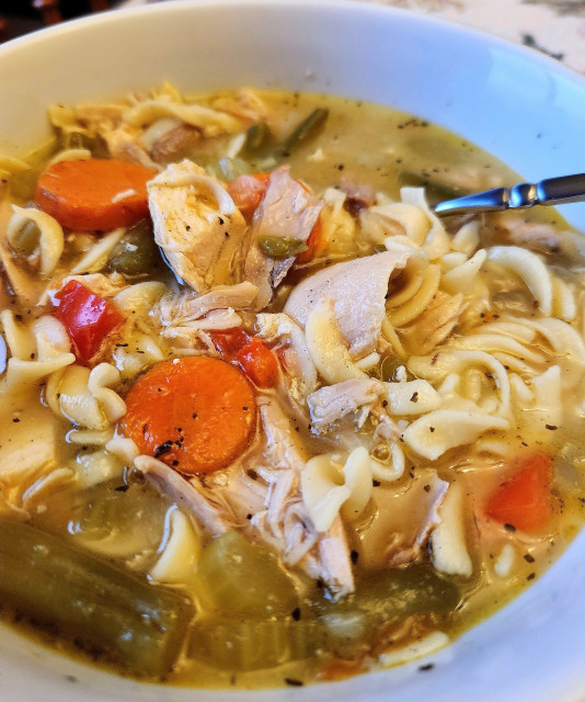 Home made chicken soup with big pieces of carrots and chicken in a white bowl.