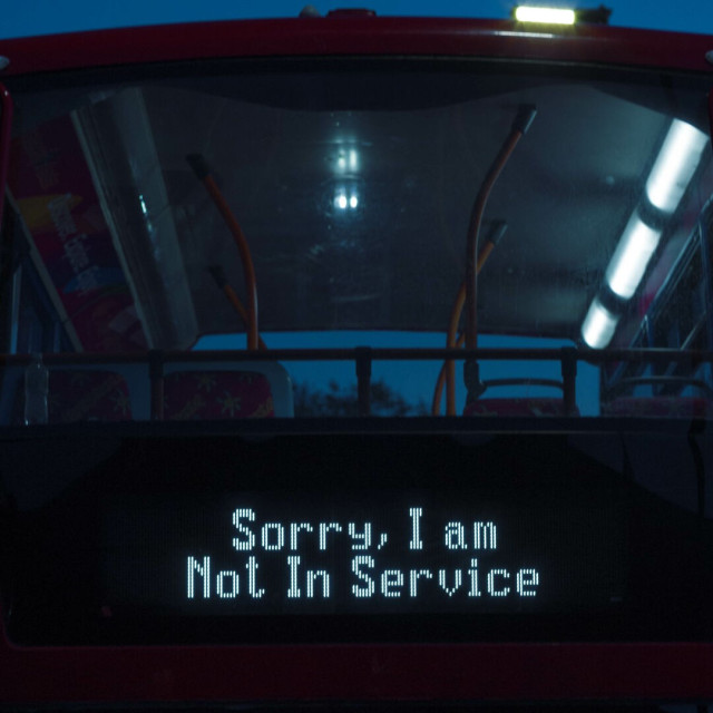 Photo of the top of the front of a red double-decker bus taken late in the evening. Through the large window across the top can be seen some orange poles meeting the ceiling, two rows of lights along the roof with only those on the right lit, the top of several seats. This interior is truncated because it's a tourist bus with a large open rear deck. Anyway, across the bottom of the image is a large black led sign, currently displaying the following in white letters: 
Sorry, I Am 
Not In Service