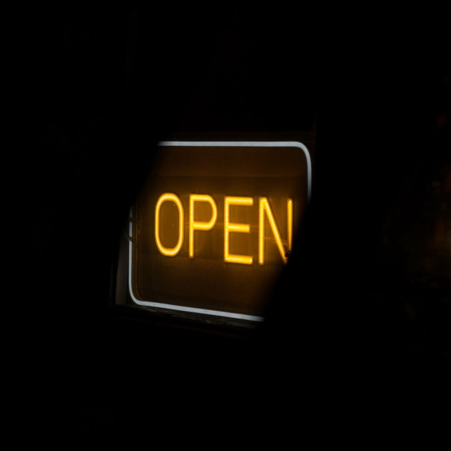 Photo of a neon-type sign that says 'OPEN' in orange, inside a white round rectangle, in the dark, obscured diagonally top-left and top-right.