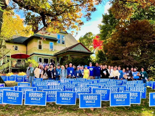 Photo of a group of volunteers in front of a building holding blue Harris/Walz signs.