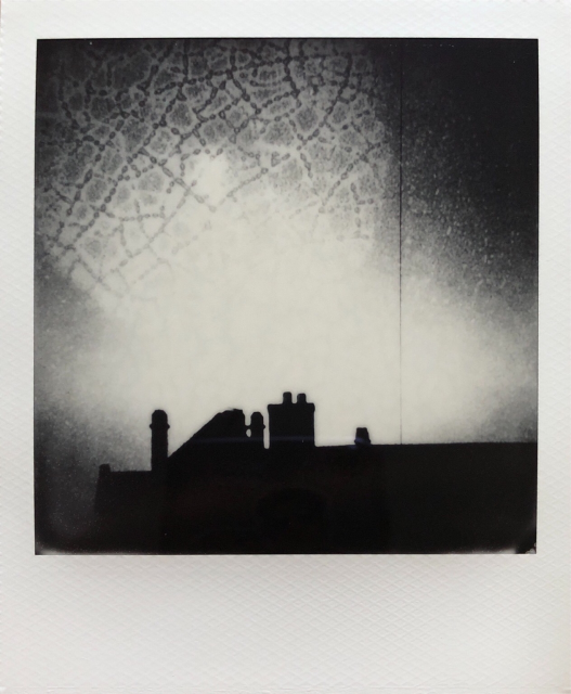 Double exposure polaroid : roofs and chimneys dark silhouettes and a water drops network in the background.  