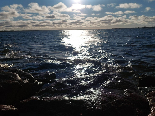 Unintentionally artistic photo of some cliffs, waves, sun, and clouds.