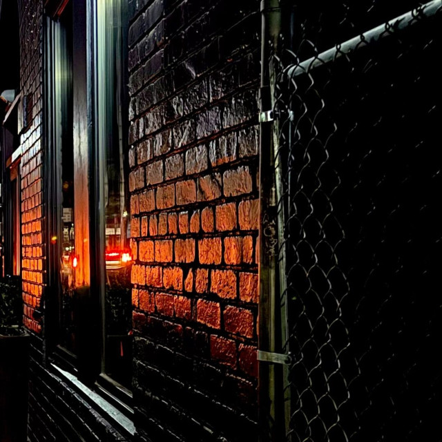 Wet brick wall with red brake lights reflecting off it.