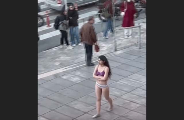 A photo of a woman in her underwear walking along a sidewalk.