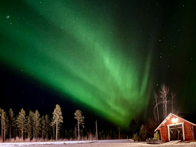 Green aurora arcs crossing the sky behind a red little outbuilding 