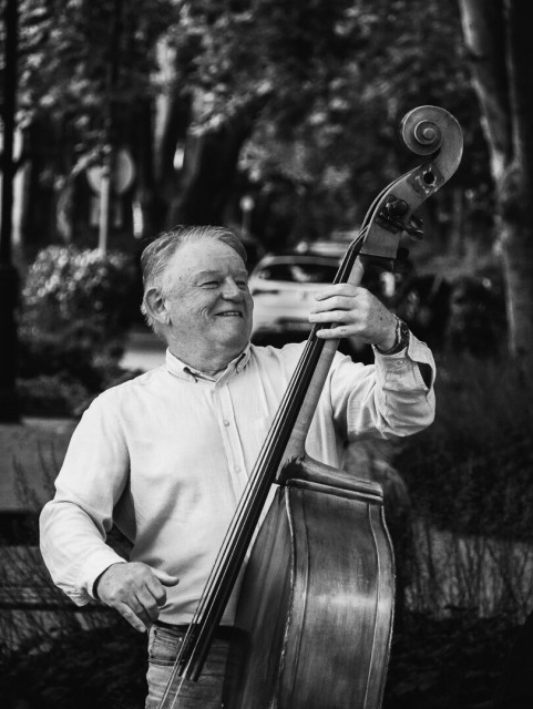 Ein älterer Herr, der einen Kontrabass mit 3 Saiten bei einem  Straßenkonzert spielt. Voller Enthusiasmus und mit freudigen Gesichtsausdruck haut er in die Saiten.