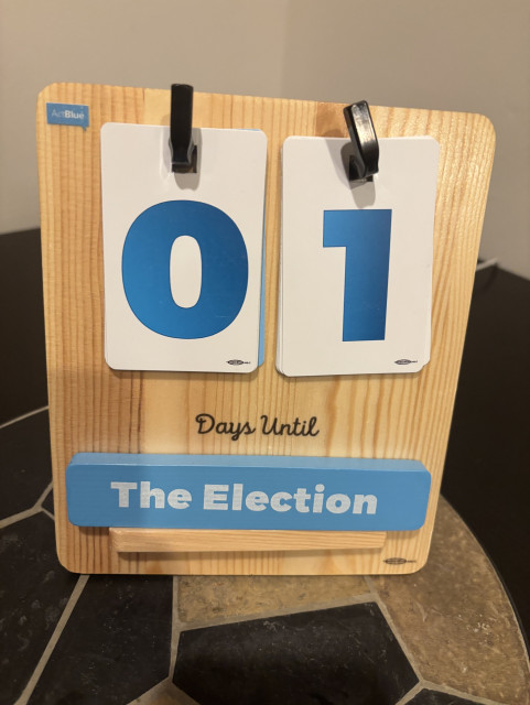 A countdown calendar reads "01 Days Until The Election" with blue and white numbers on a wooden stand.