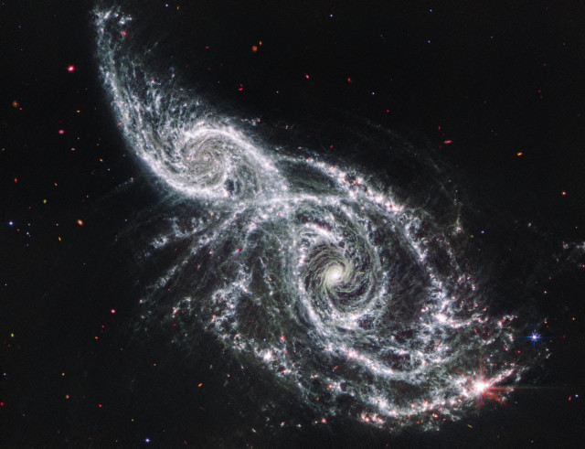 Webb’s mid-infrared image excels at showing where the cold dust glows throughout these galaxies — and helps pinpoint where stars and star clusters are buried within the dust. Find these regions by looking for the pink dots along the spiral arms. Many of these areas are home to actively forming stars that are still encased in the gas and dust that feeds their growth. Other pink dots may be objects that lie well behind these galaxies, including extremely distant active supermassive black holes known as quasars.