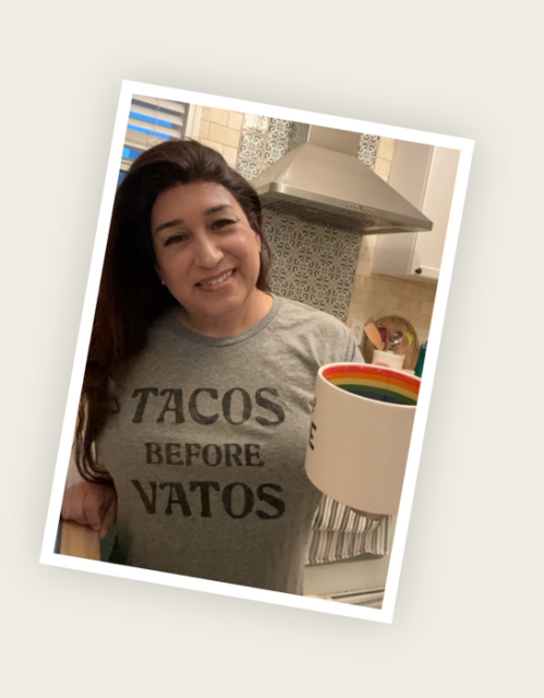 Me, a trans femme Latine enby woman, holding a coffee mug with a rainbow stripe inside it. 

I am wearing a gray t-shirt that reads “Tacos before vatos”