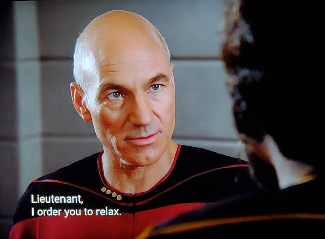 TNG scene. We're on the bridge, I think on that cute lil' ramp that runs to the upper back bridge from the lower front bridge. 
Picture 1 shows Picard close in, standing in conversation with Worf, an gruff and burly alien with ridged forehead loaf. Point of view indicates Picard is speaking. Closed caption reads, "Lieutenant, I order you to relax."
Pic 2 shows Worf, visibly intense and looking like he wants to strike down upon thee with great vengeance and furious anger, responds,"I am relaxed."
Pic 3 shows Picard, looking shooketh and taken aback. No caption.