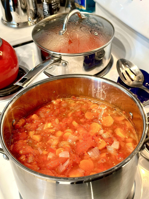 Closer view of the foreground pot slowly simmering tomatoes and other veggies to become spaghetti sauce. Farther back there is a 3 quart pot simmering tomato peels to be strained for tomato juice. 