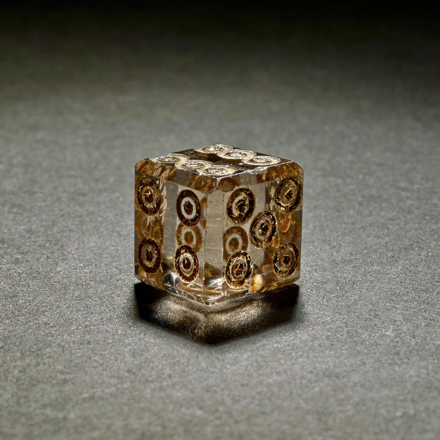 Crystal die with six sides, each pipped in the modern arrangement with circled dots. The edges are slightly beveled and it is transparent with a slight amber tint.

https://www.britishmuseum.org/collection/object/G_1772-0311-220