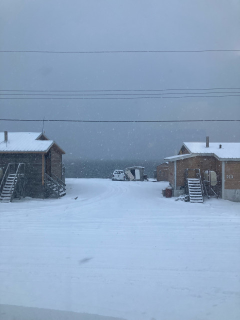 A view out my kitchen window. There is a heavy snowfall and between the two houses across the street the dark ocean can be made out but the rest of the scene is simply grey. 